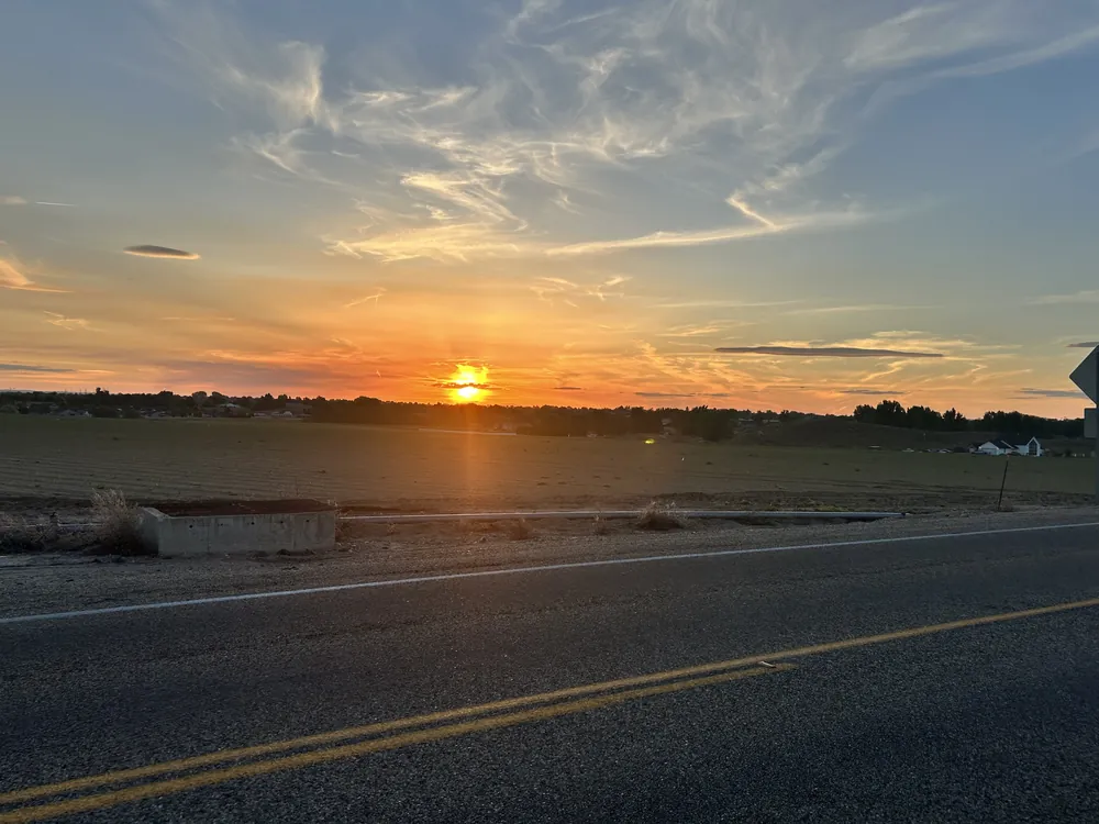 The sun setting over open fields beside a quiet road